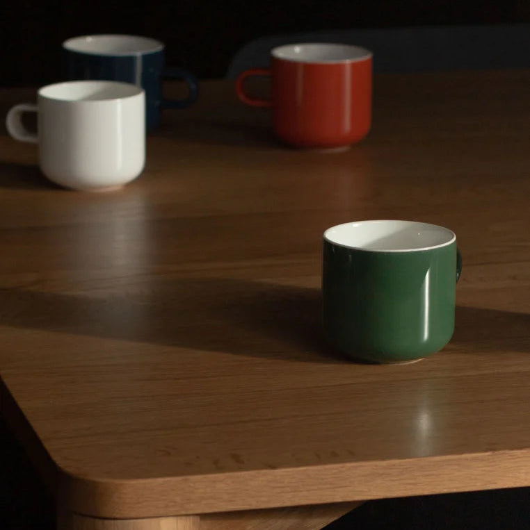 Four Acme Bobby Mugs in Kōkako, Clay, and Kawakawa colours arranged on a wooden table with a dark background — Aunty Tommy&