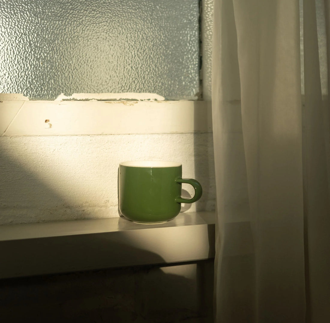 Green mug on a windowsill with soft lighting