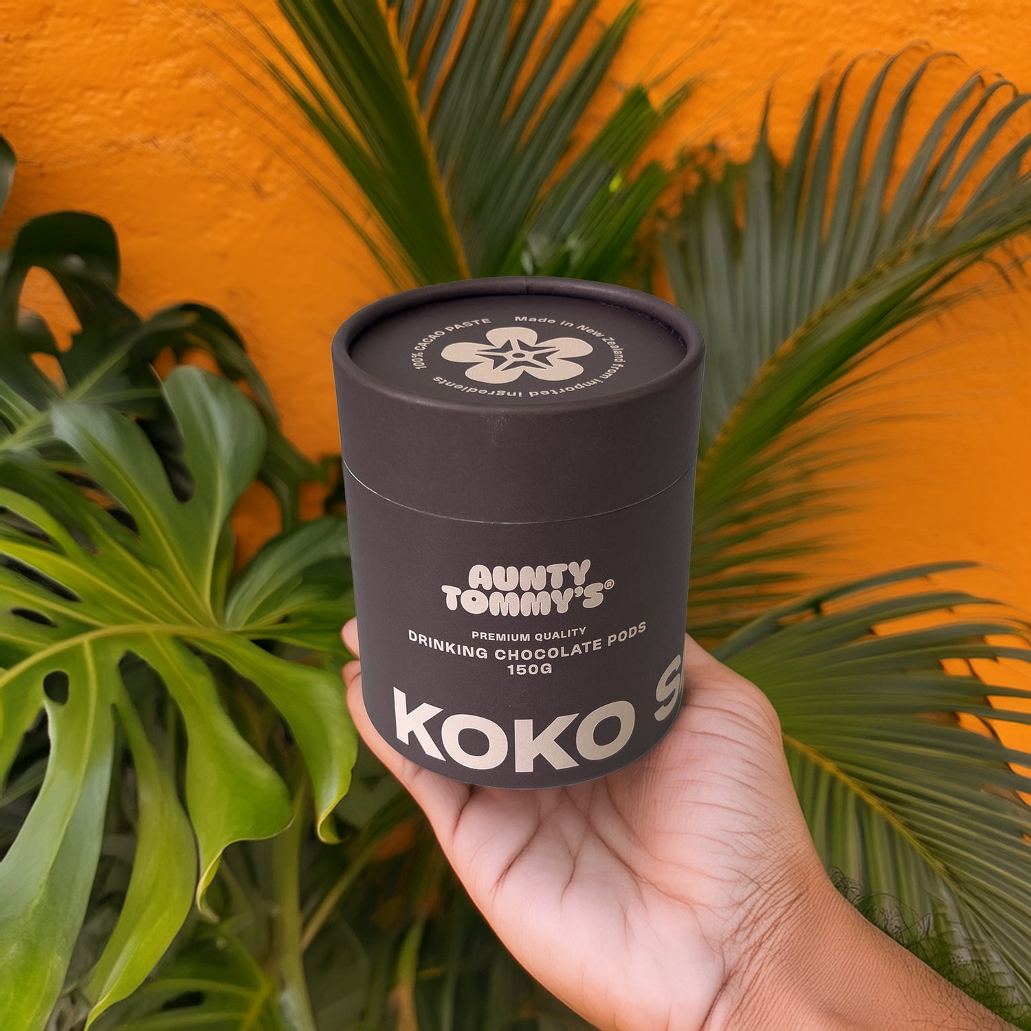 Koko Samoa Drinking Chocolate Pods container being held in a hand in front of an orange wall