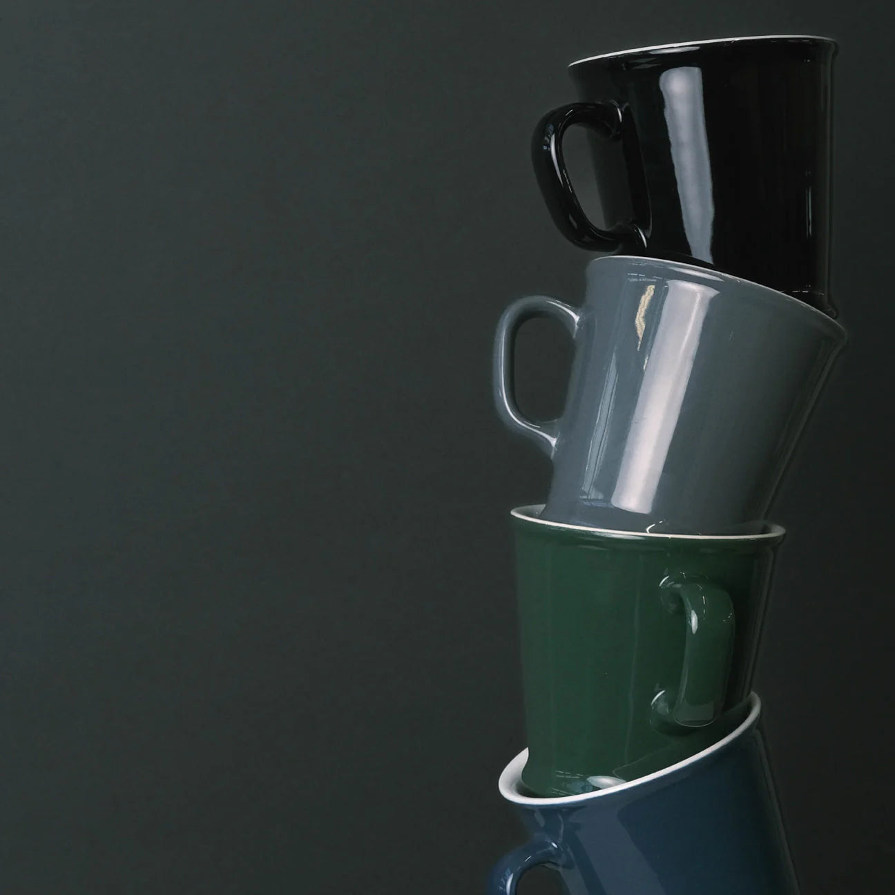 Stack of three mugs in black, gray, and green on a dark background